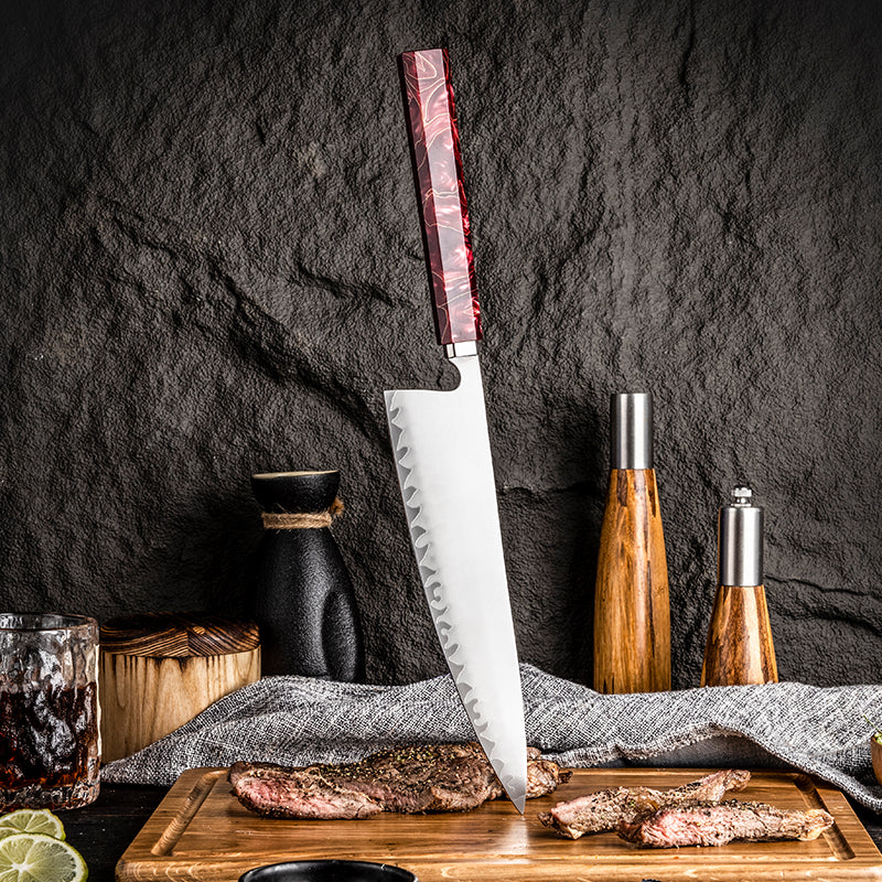 Forked kitchen knife with red handle with a wooden handle on a cutting board with cooked meat, against a dark stone wall.