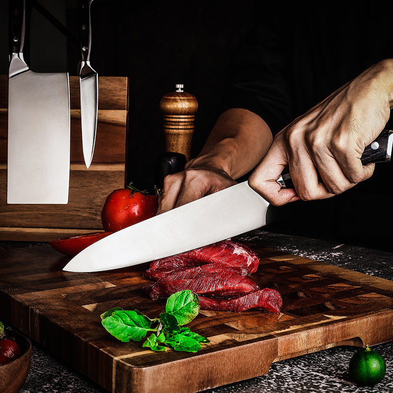 Person cutting raw meat on a wooden cutting board with a professional german steel knife, surrounded by ingredients.