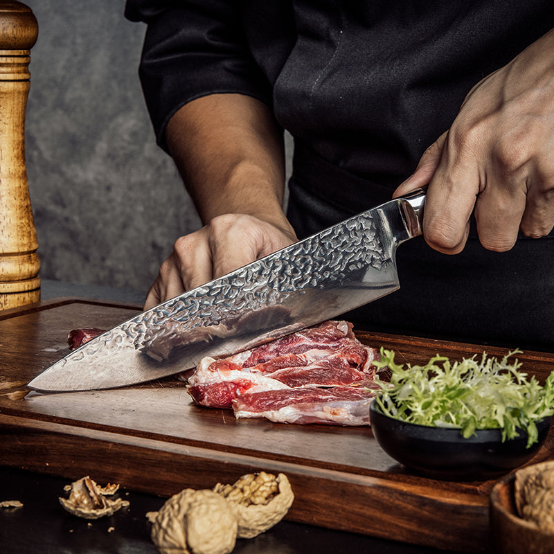Person cutting meat on a wooden board with a large knife, surrounded by ingredients.