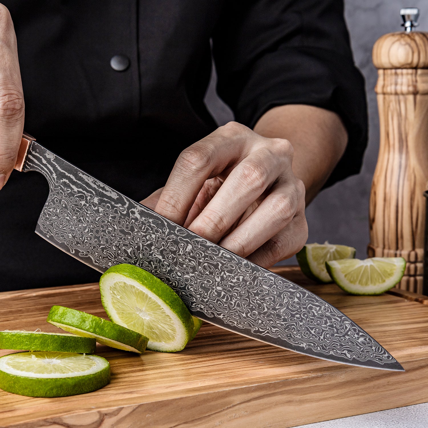 Person holding a Damascus knife over sliced limes on a wooden cutting board.