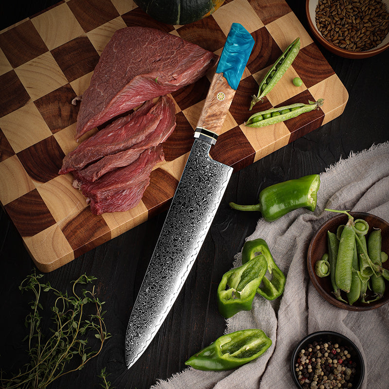 Wooden cutting board with raw meat, a chef's knife, and green peppers on a dark surface.