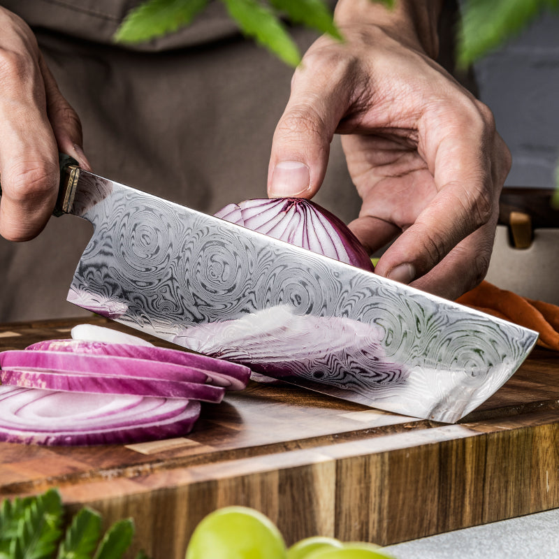 Person slicing a red onion with a decorative nakiri knife on a wooden cutting board.