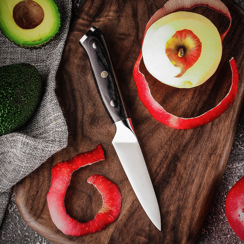 Wooden cutting board with a knife, sliced red pepper, and whole avocado on a textured surface.