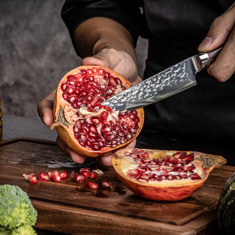 Person cutting a pomegranate on a wooden cutting board with a japanese Hikari knife.