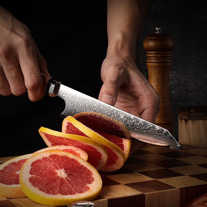 Person slicing a grapefruit with a small japanese knife on a wooden cutting board.