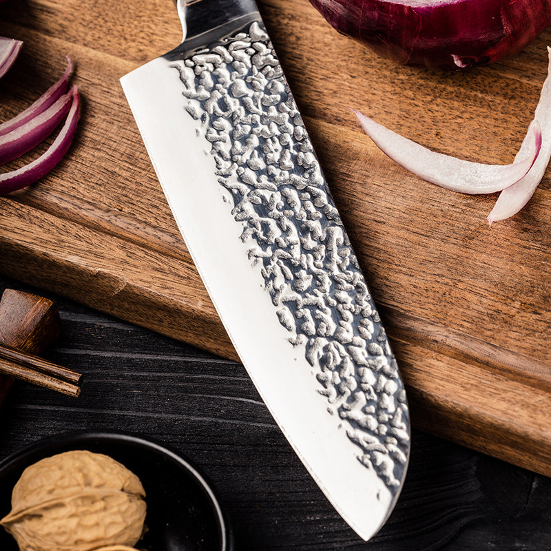Stainless Steel Hikari Santoku kitchen knife with textured blade on a wooden cutting board with onions and spices.
