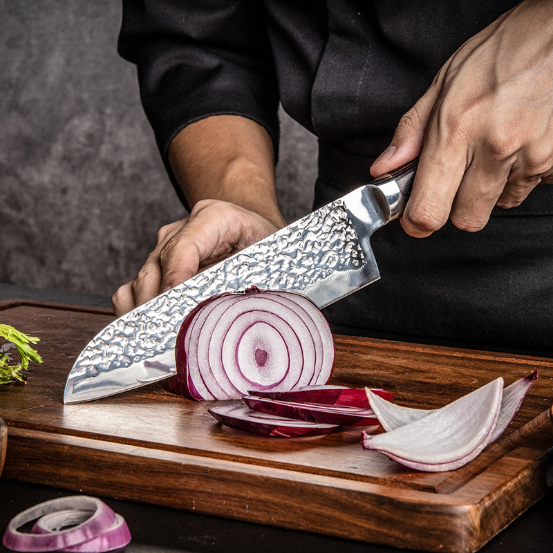 Person slicing red onions on a wooden cutting board with a chef's knife.