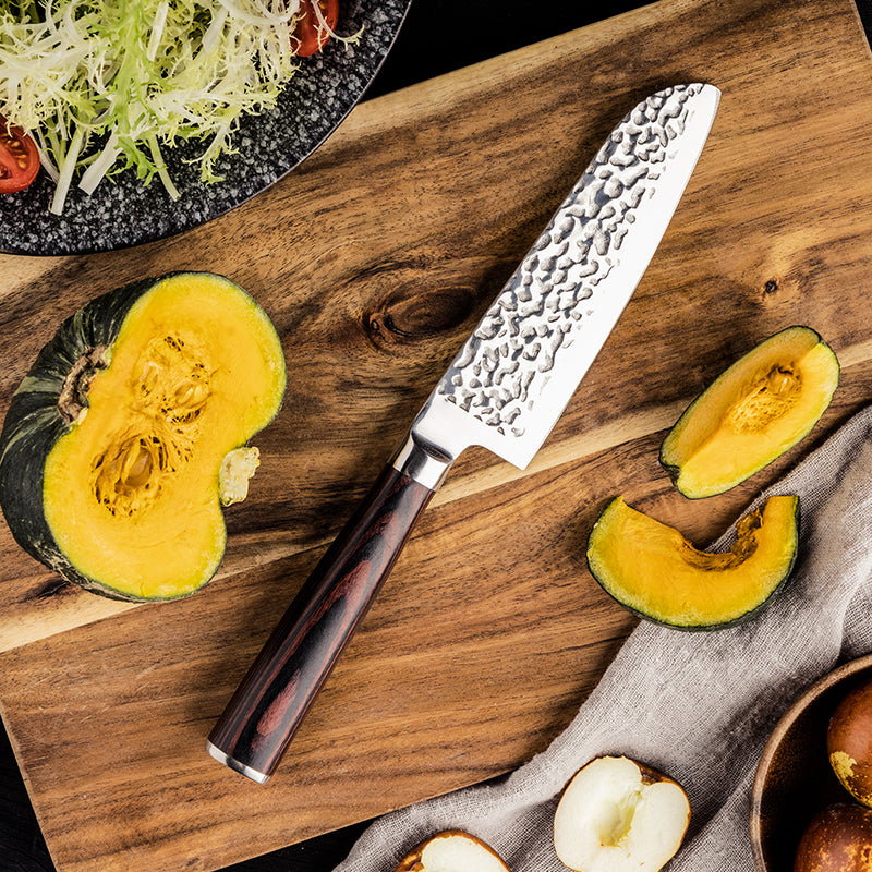 Hikari Small Santoku knife on a wooden cutting board with sliced squash and salad ingredients.