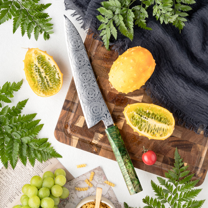 Decorative Rose Damascus Pattern knife with green handle on a wooden cutting board with fruits and leaves.