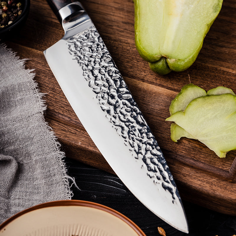 Chef's knife with a textured blade on a wooden cutting board with sliced green apples.