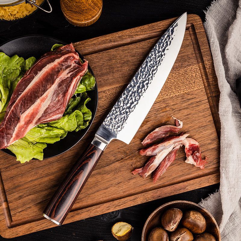Wooden cutting board with a chef's knife, raw meat, and salad leaves on a dark surface.