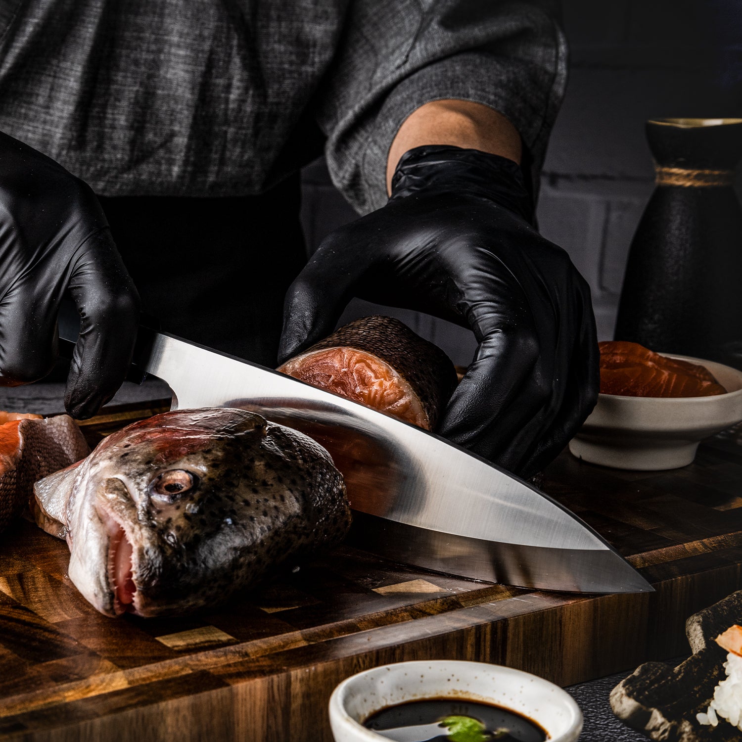 Professional fish knife Hikari Knife Japanese Chef in black gloves cutting a fish on a wooden board with a dark background