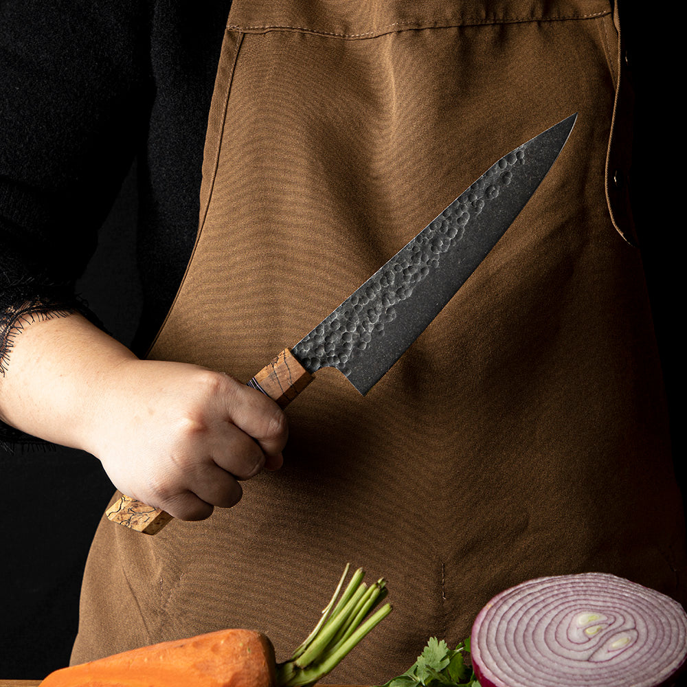 Professional knife held by chef near onion and carrot