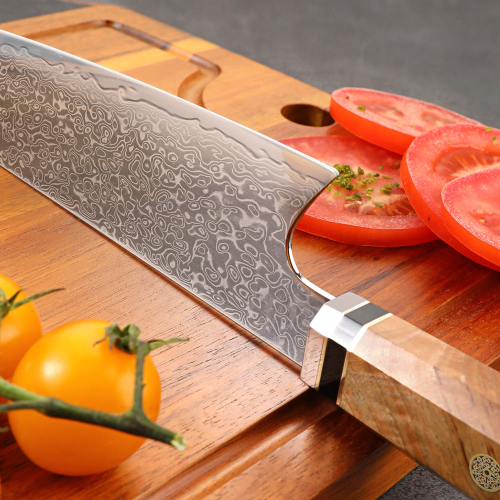 Chef's knife with a decorative blade on a wooden cutting board with sliced tomatoes