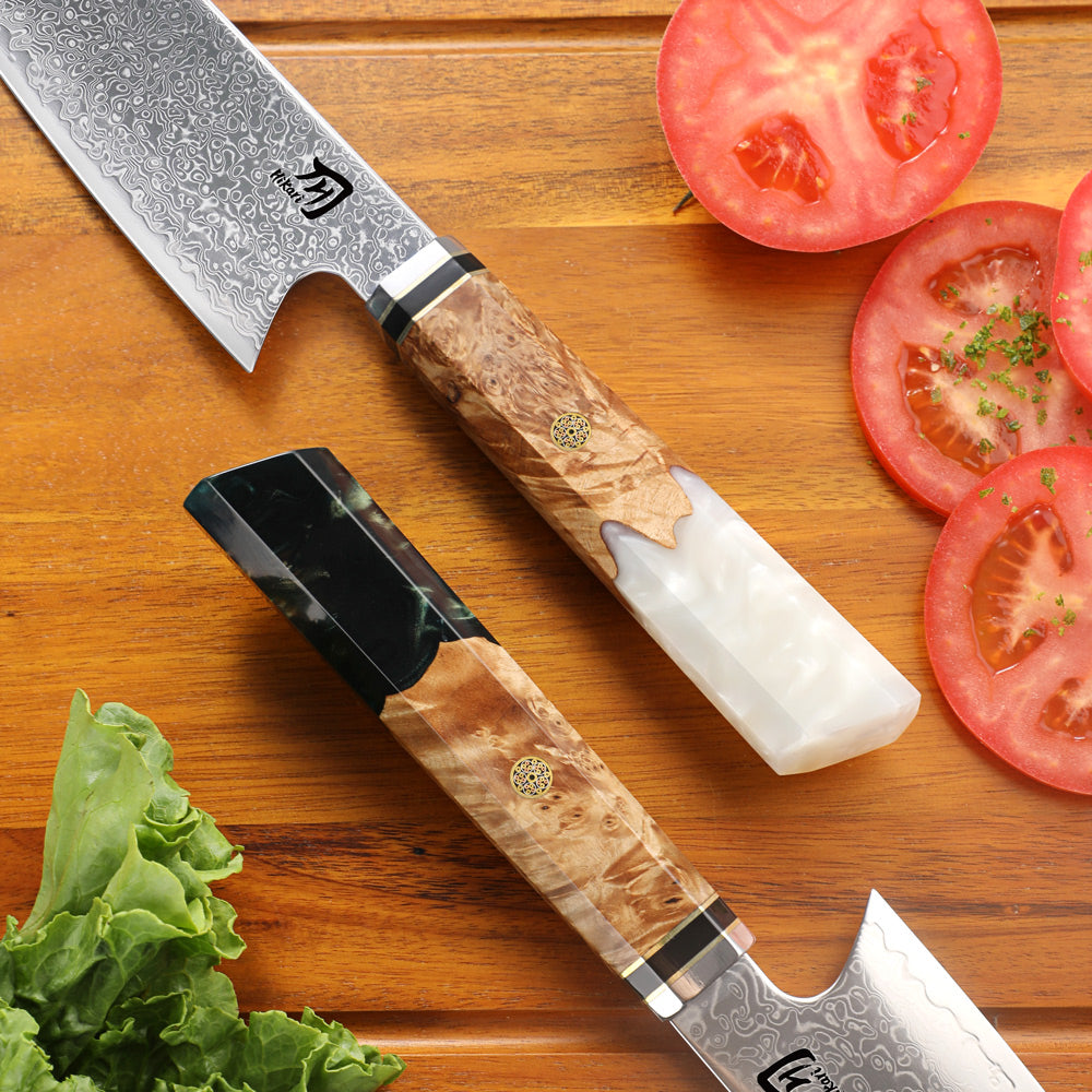 Two chef's knives with wooden handles on a wooden surface with sliced tomatoes and lettuce.