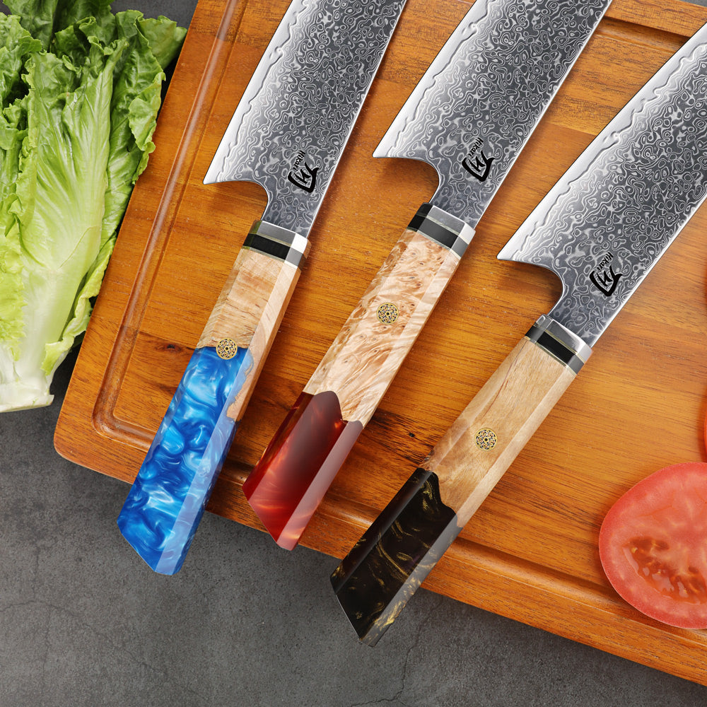 Three Damascus steel kitchen knives with wooden handles on a cutting board with vegetables.