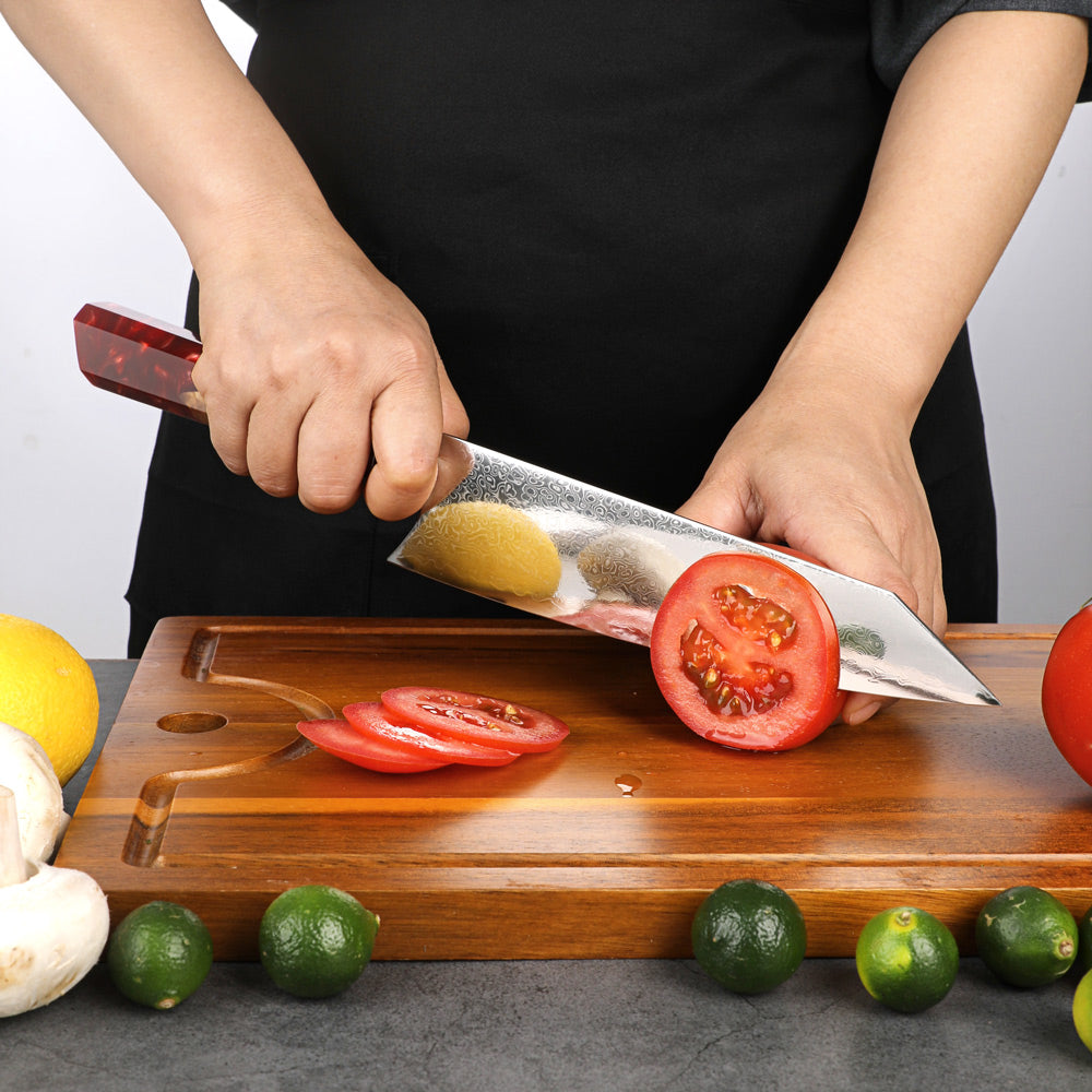 Person cutting tomatoes on a wooden board with a knife, surrounded by limes and garlic.
