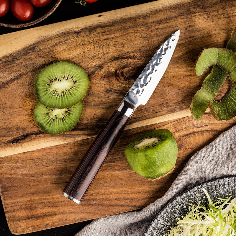 Sliced kiwis on a wooden cutting board with a japanese small utility knife