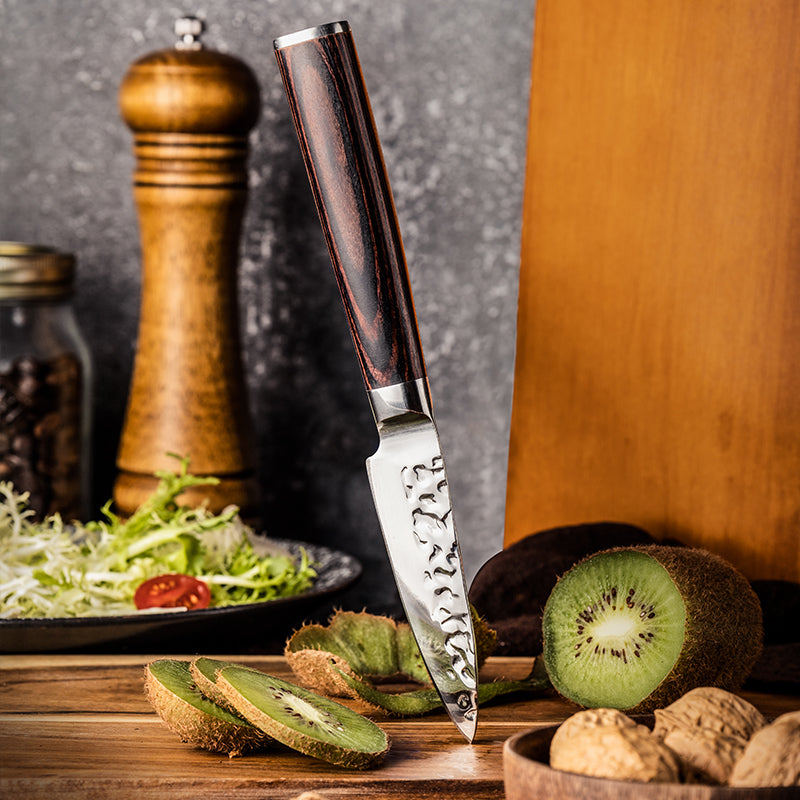 Knife on a wooden cutting board with sliced kiwis, walnuts, and a salad in the background.