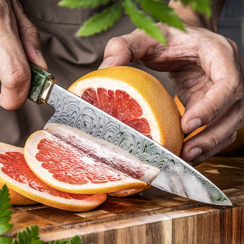 Person cutting a grapefruit with a decorative knife on a wooden cutting board.