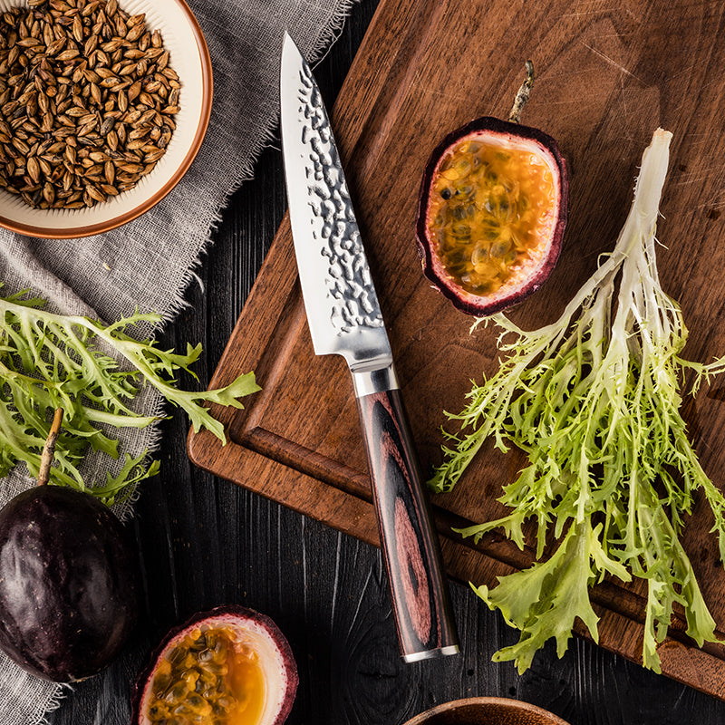 Wooden cutting board with small stainless steel knife, passion fruit halves, and leafy greens on a dark surface.