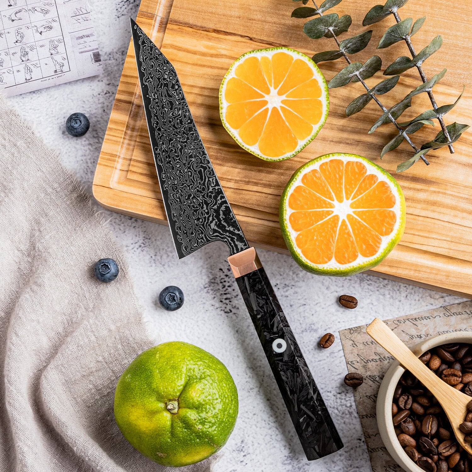 Utility knife on a wooden cutting board with sliced oranges, a lime, and coffee beans.