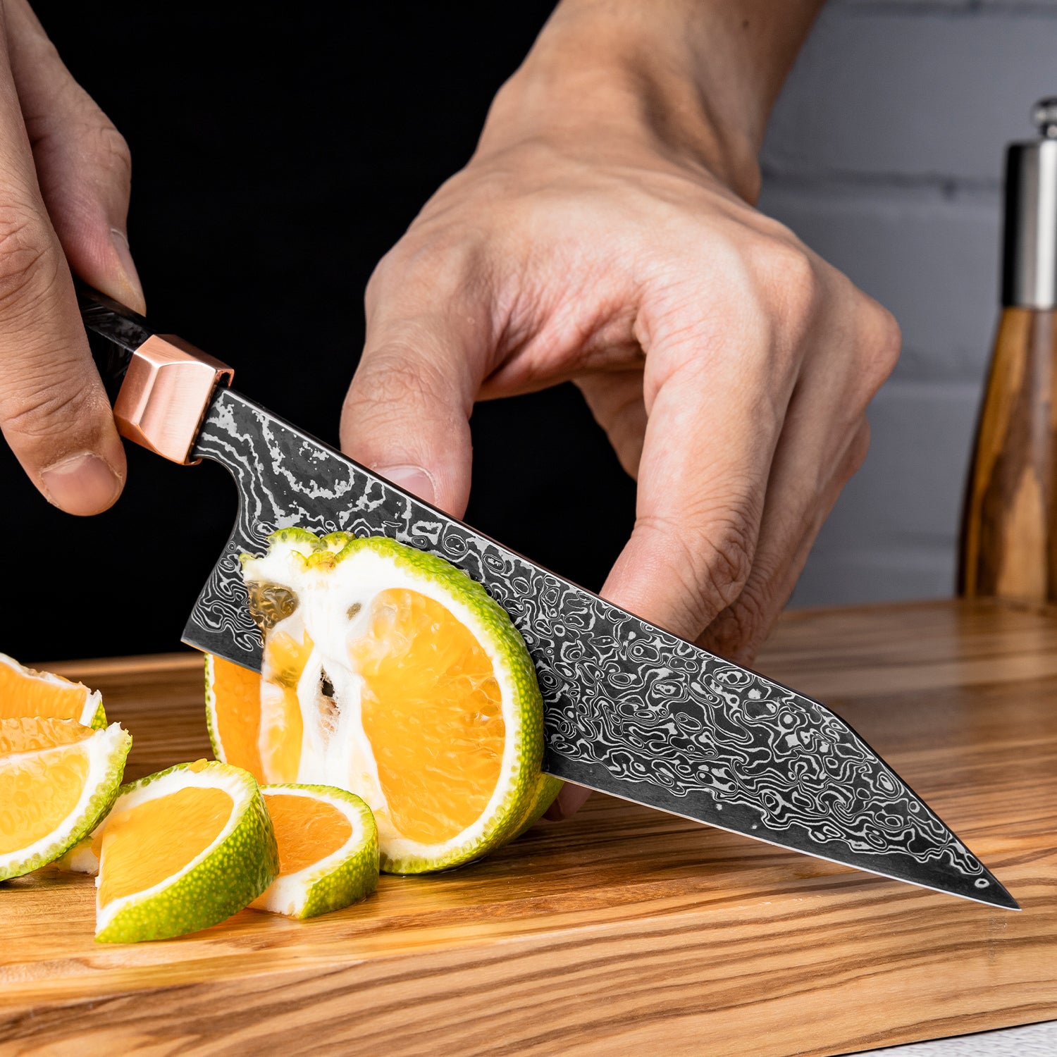 Person using a decorative small knife to cut oranges on a wooden cutting board.