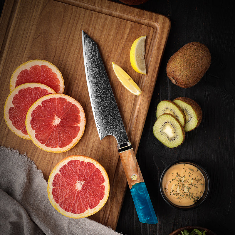 Wooden cutting board with sliced grapefruit, kiwi, and lemon, featuring a japanese utility knife.