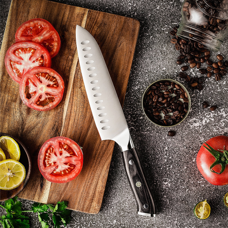 Wooden cutting board with sliced tomatoes, a japanese professional and sharp knife, and coffee beans on a dark surface.