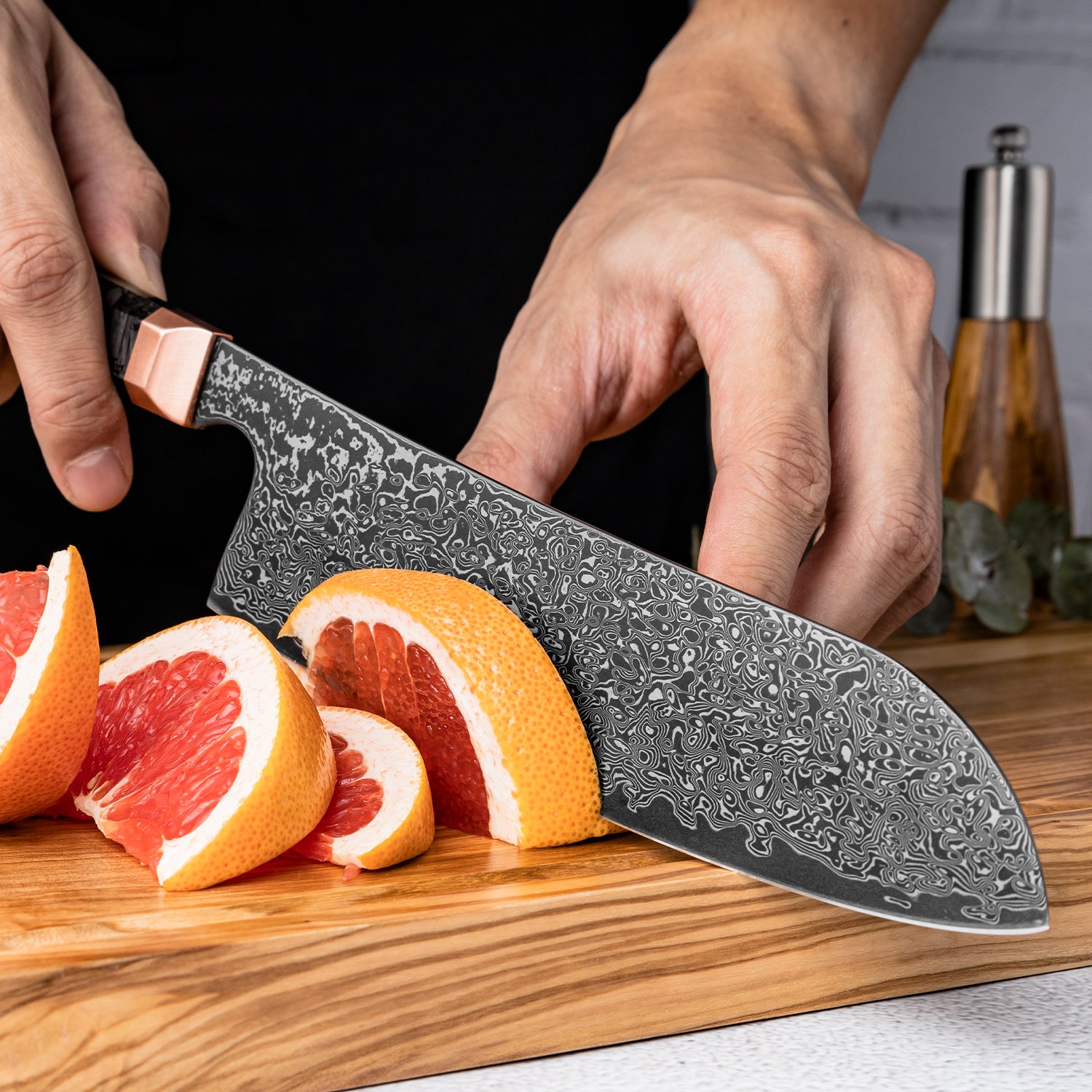 Person using a Damascus all purpose santoku knife to cut grapefruits on a wooden cutting board.