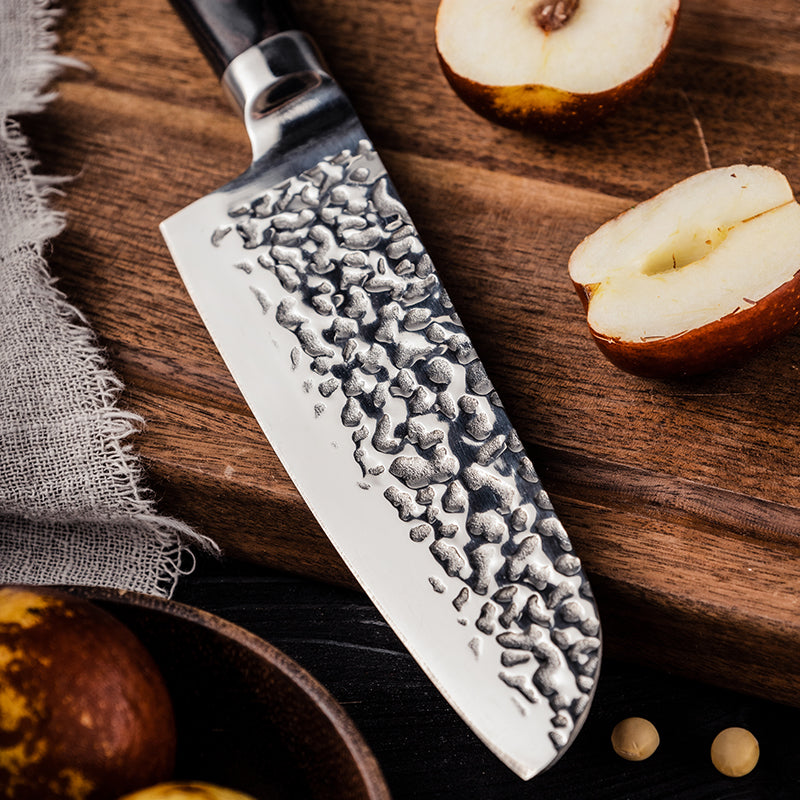 Chef's knife with textured blade on a wooden surface with apples