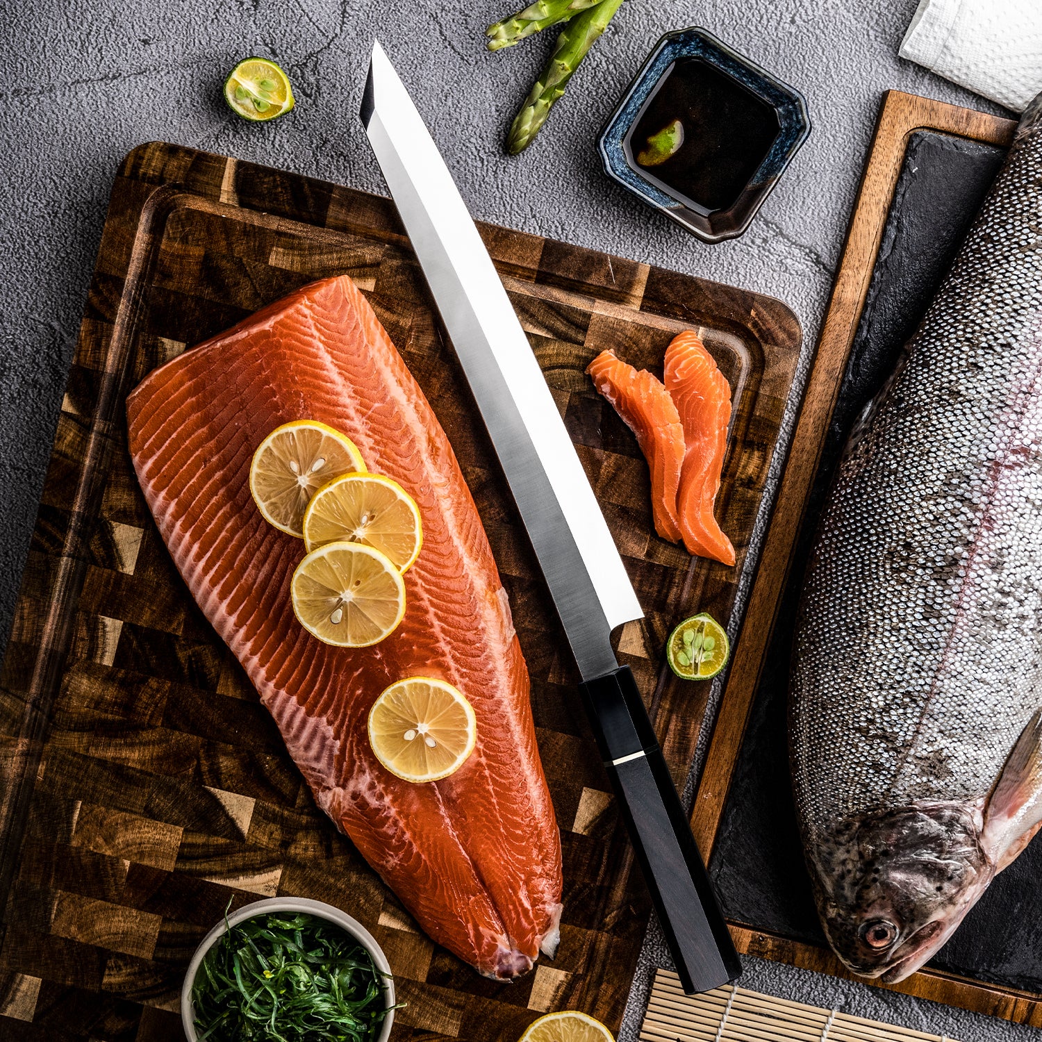Raw salmon fillet with lemon slices on a wooden cutting board, accompanied by a Hikari Knife kitchen knife for fish yanagiba premium materials and very sharp and other ingredients.